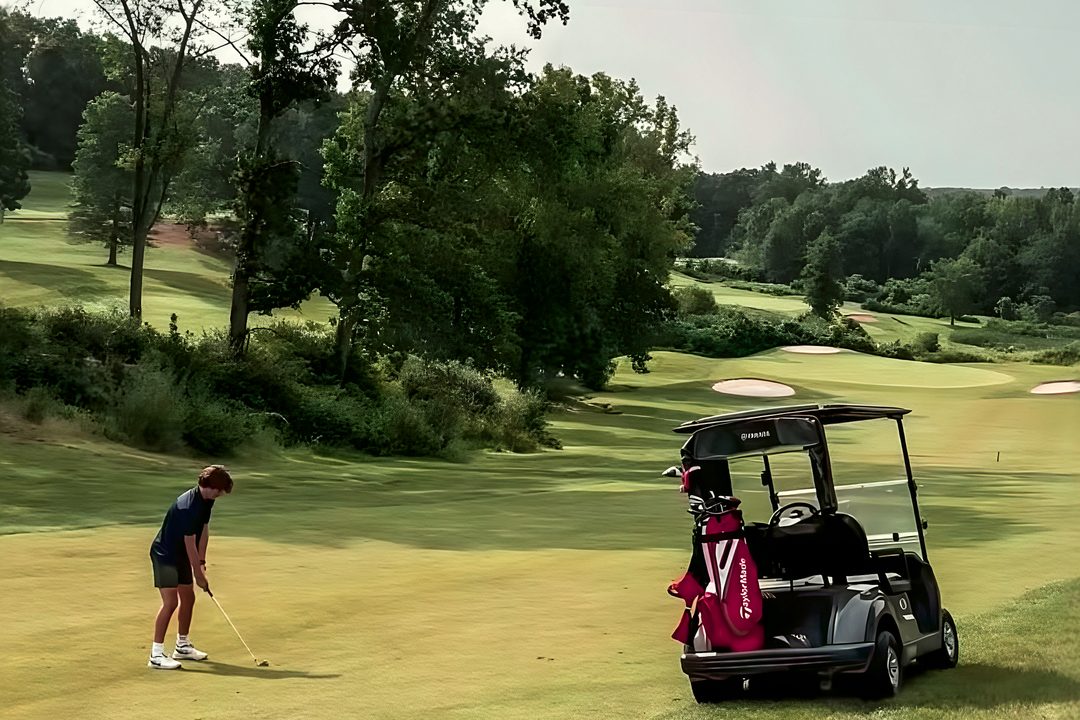 Golfer chipping beside a golf cart during a charity outing at The VUE