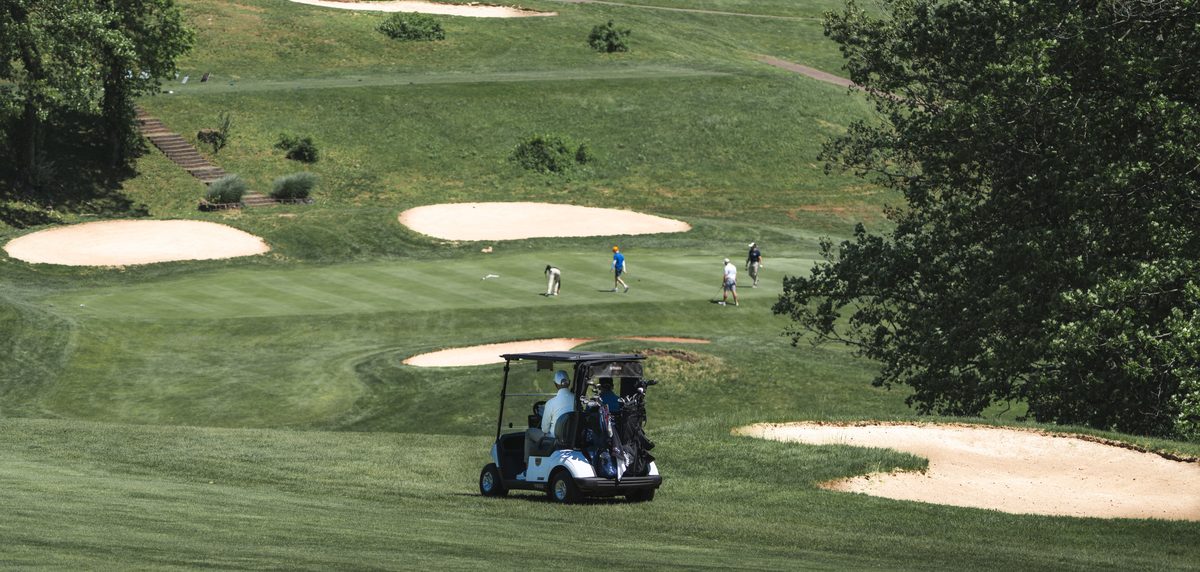 Golf cart on a fairway lined with sand bunkers as golfers play the green at The VUE