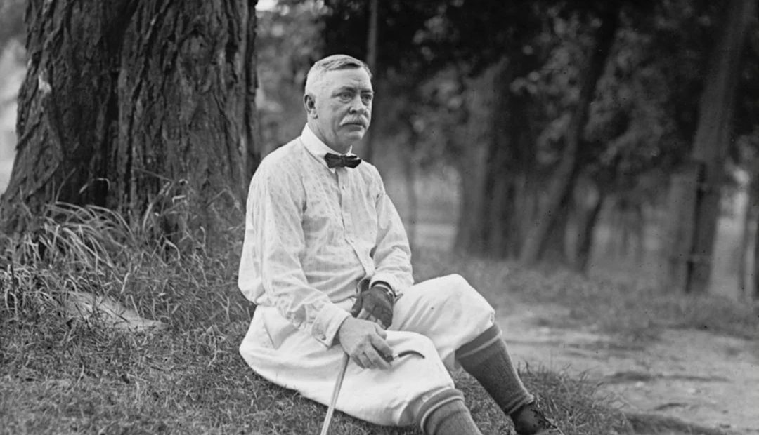 Vintage black-and-white photo of a golfer in knickers seated beneath a tree, from the course's early history