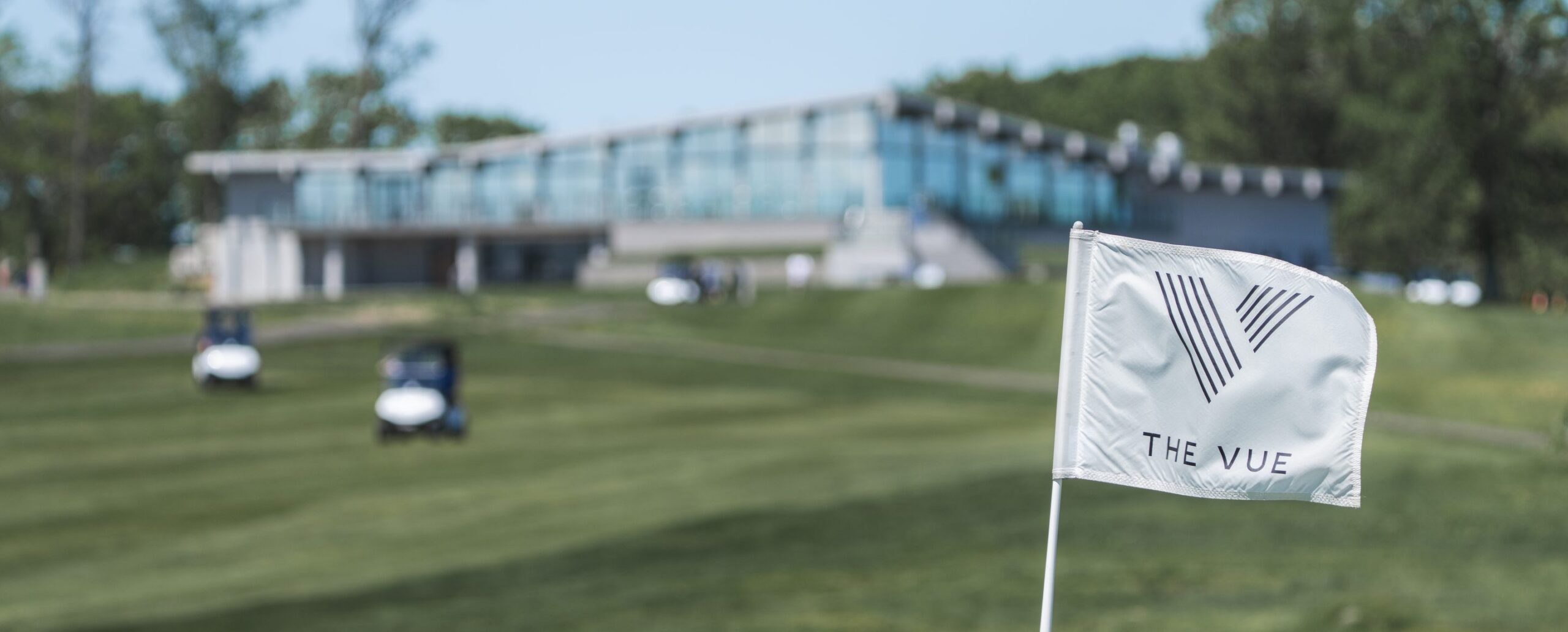The VUE logo flag on the golf course with the glass clubhouse and golf carts in the background